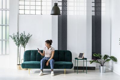 Young businesswoman using smart phone while sitting on sofa at creative workplace