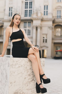 Portrait of young woman sitting on street in city