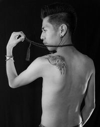 Rear view of shirtless man wearing bead necklace against black background