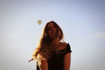 Low angle view of smiling young woman against hot air balloon