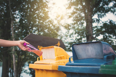 Cropped image woman throwing bottle in garbage bin