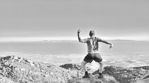 Full length of man standing on rocks by sea against sky