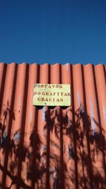 Low angle view of sign on corrugated iron during sunny day