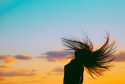 Silhouette woman tossing hair against sky during sunset