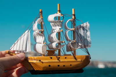 Close-up of hand holding sailboat against clear sky