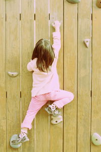 Rear view of girl practicing rock climbing on wood wall