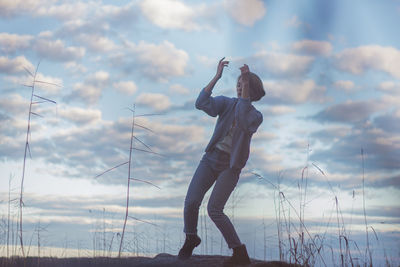 Young woman dancing on rock against cloudy sky