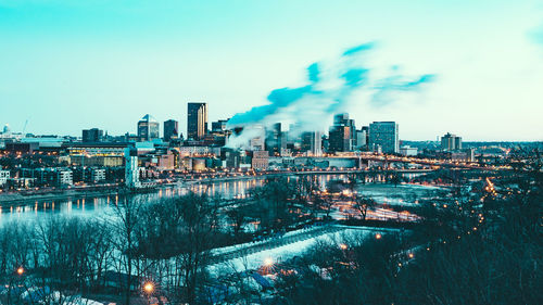 Smoke emitting from illuminated city against sky