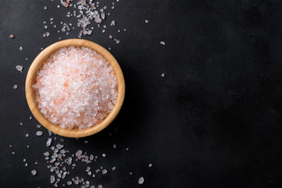 Pink himalayan salt in a wooden bowl with scattered salt on a black background, copy space