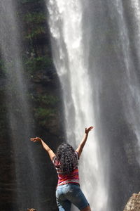 Rear view of woman with arms raised on rock