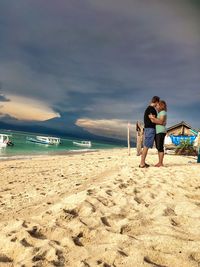 Full length of couple embracing at beach against sky