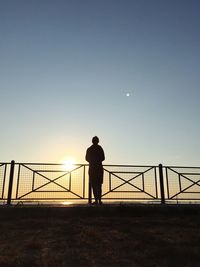 Woman walking on bridge against clear sky during sunset