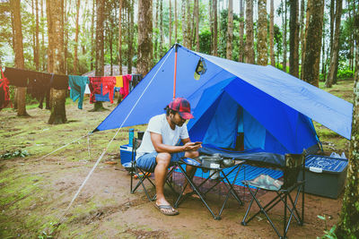 Man sitting by tent in forest