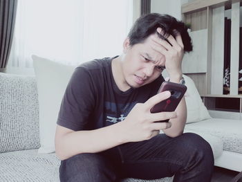 Tensed young man using smart phone while sitting on sofa at home