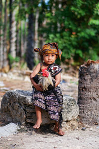 A child wearing traditional clothes holding a rooster to take part in a traditional festival 