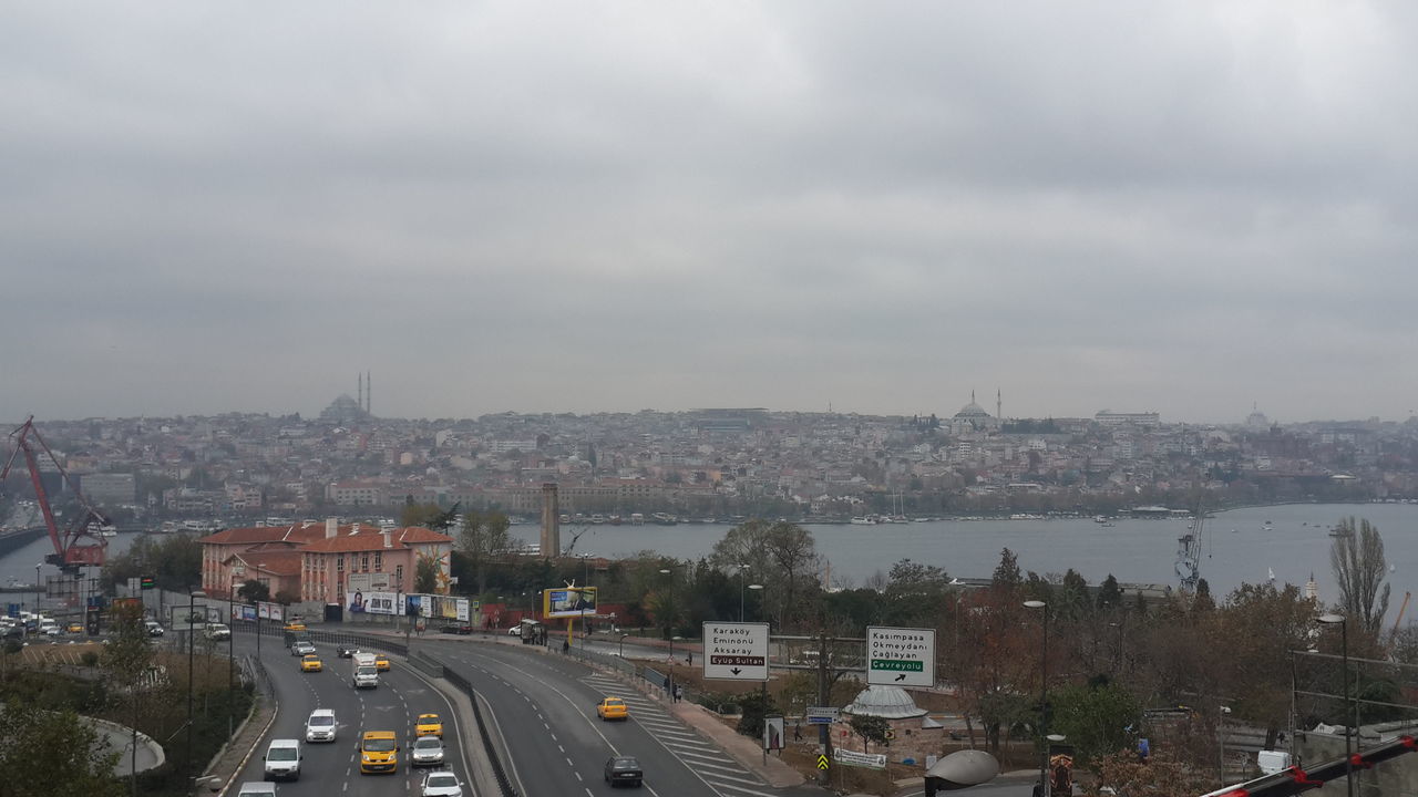 city, building exterior, architecture, built structure, transportation, sky, high angle view, cityscape, road, car, cloud - sky, street, land vehicle, cloudy, mode of transport, overcast, city life, weather, outdoors, residential district