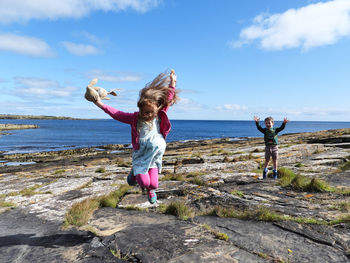 Girl standing on rock by sea against sky
