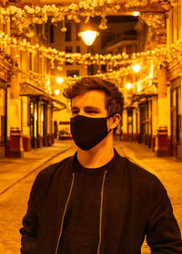 Portrait of young man standing on illuminated street at night