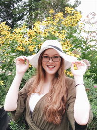 Portrait of cheerful young woman wearing hat while standing against yellow flowers