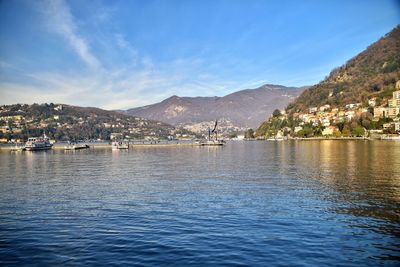 Sailboats in lake by city against blue sky