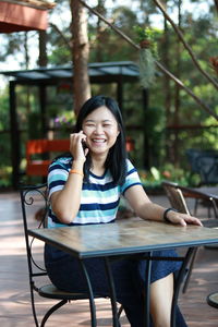 Portrait of young woman using mobile phone while sitting on table