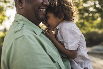 Midsection of happy father embracing son while standing at park