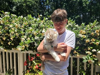 Gen z teen holds shorkie puppy outdoors.