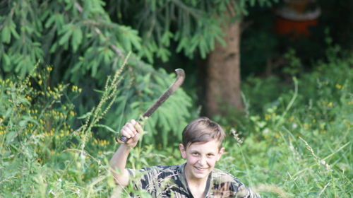 Portrait of boy smiling while holding knife amidst plants