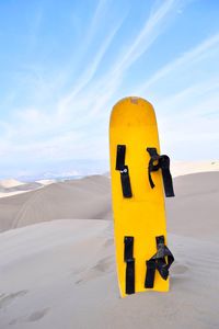 Close-up of yellow signboard on sand against sky