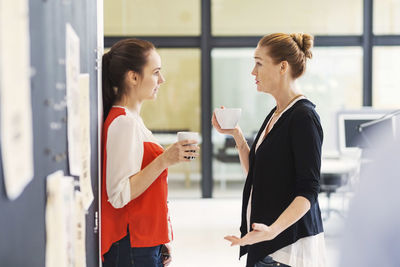Side view of businesswomen discussing while having coffee in office
