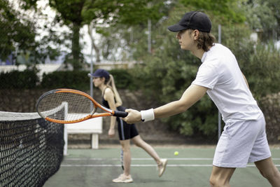 Side view of two concentrated tennis players on tennis court ready to hit the ball close to the net