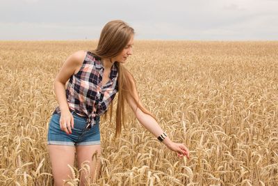 Full length of young woman standing in wheat field against sky
