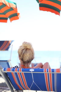 Rear view of woman relaxing on lounge chair at beach