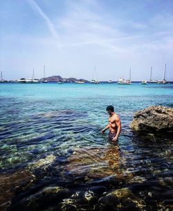 Full length of shirtless man on sea against sky