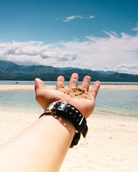 Low section of hand on beach against sky