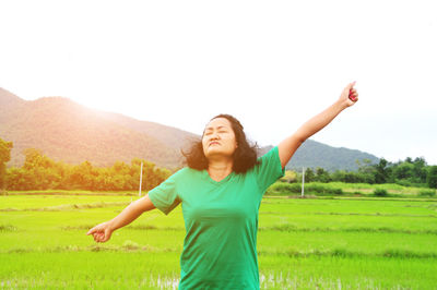 Woman stretching arms on field against sky