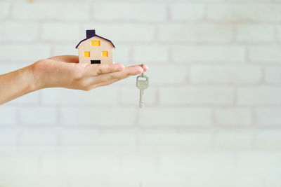 Close-up of cropped hand holding model home with key against brick wall