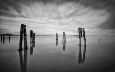 Wooden posts in sea against sky at dusk