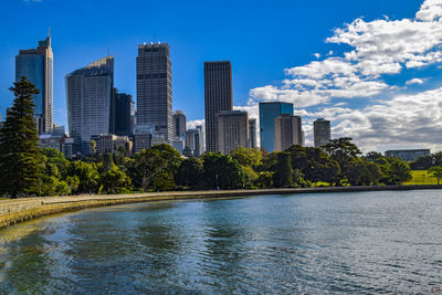 Modern buildings by river against blue sky
