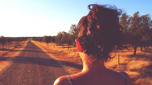 Rear view of woman on street amidst trees against sky