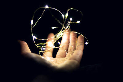 Close-up of hand holding illuminated string light against black background