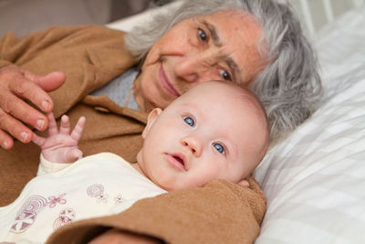 Portrait of woman with grandchild lying on bed at home