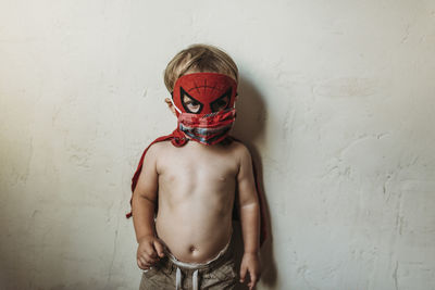 Midsection of shirtless boy standing against wall