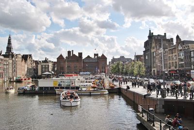 Boats in river by cityscape against sky