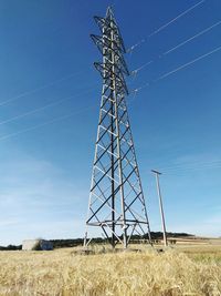 Low angle view of electricity pylon on field against clear blue sky
