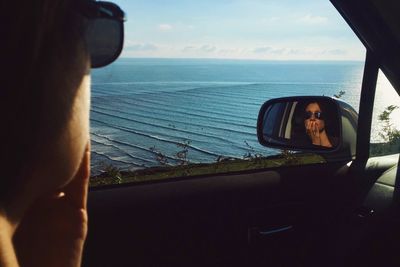 Reflection of a woman wearing sunglasses in a car wing mirror