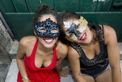 Portrait of two seated women wearing mask against green door.