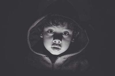 Close-up portrait of cute boy wearing hooded jacket in darkroom