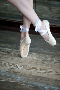 Low section of woman wearing ballet shoe on wooden floor