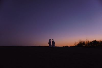 Silhouette men standing on land against sky during sunset